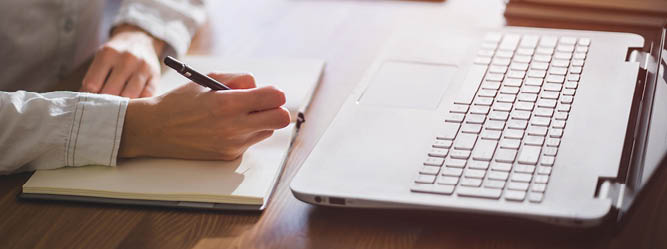 Man writing in notebook in front of open laptop
